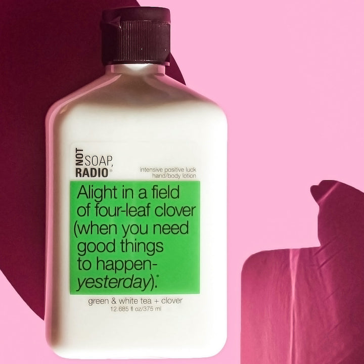 A green tea and white tea green clover scented hand and body lotion on top of a pink background.