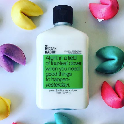 A good luck four leaf clover scented lotion laying next to colored fortune cookies.