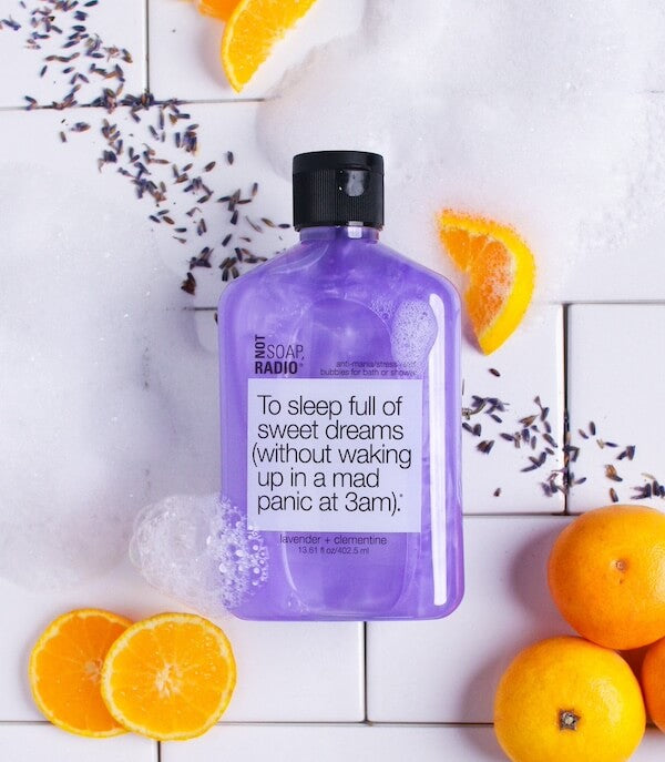 To sleep full of sweet dreams bubble bath flat laid on a tile background surrounded by lavender petals and clementines.