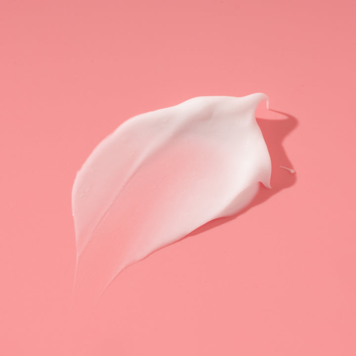 Product swatch of white body butter formula, rich in Argan oil, shea butter, and avocado oils - photographed on a pink background