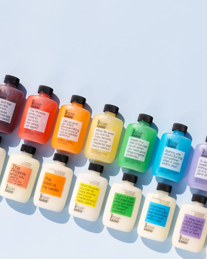 Rows of sample-sized bubble baths and lotions by Not Soap Radio, in the shape of a rainbow.