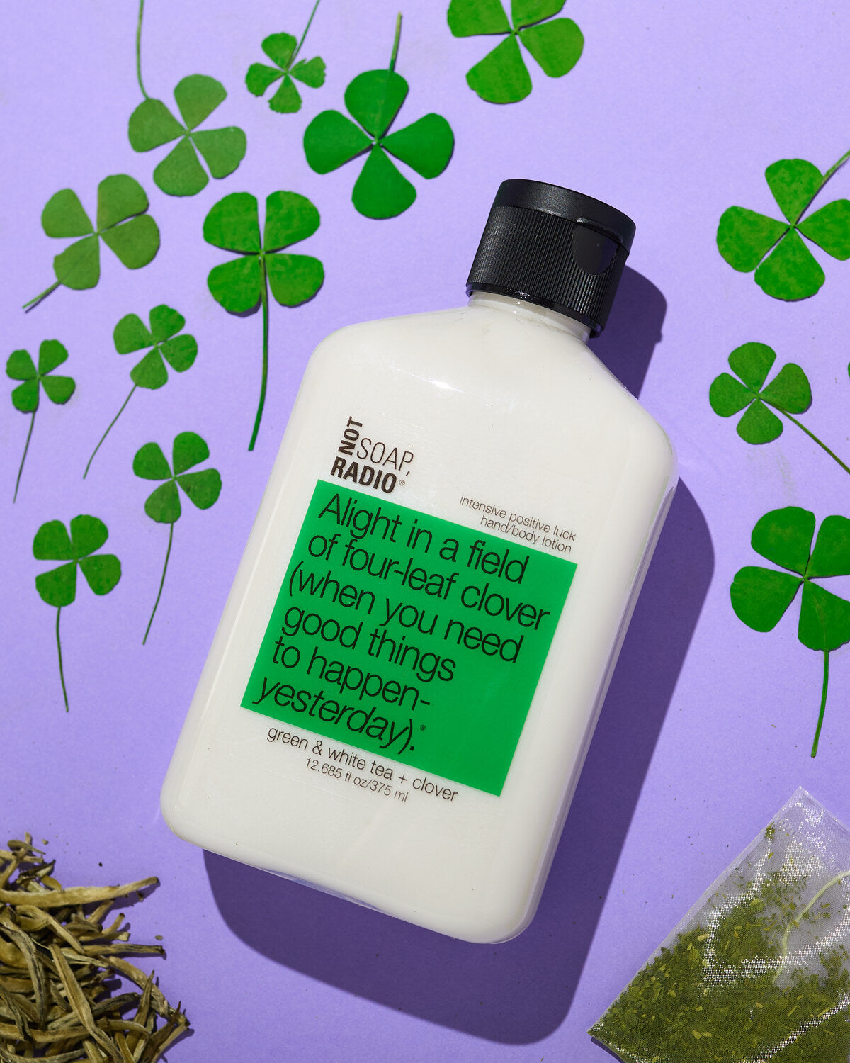 Good luck lotion, surrounded by four leaf clovers and tea bags. 