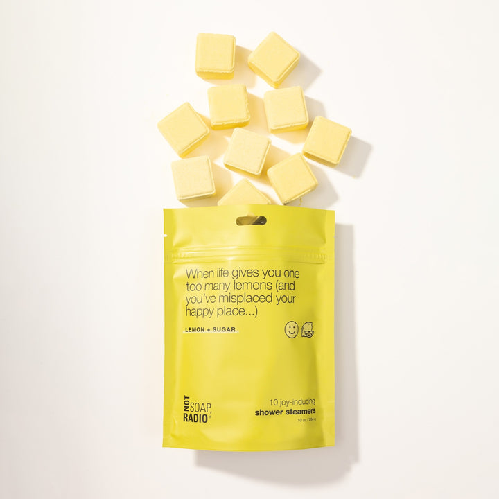 Flatlay of When life gives you one too many lemons Shower Steamers pouch, with yellow shower steamer tablets coming out of bag