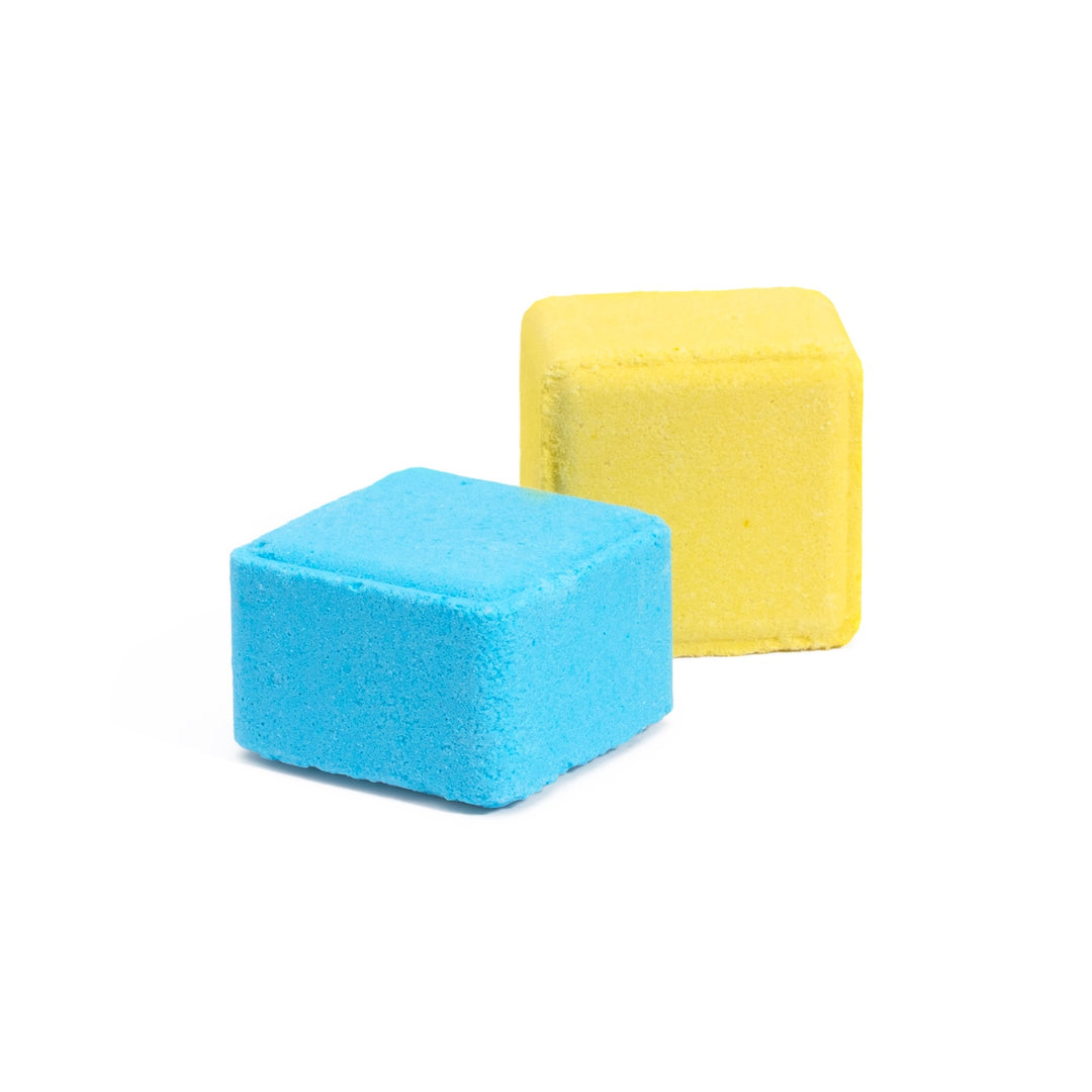 Close-up of 2 shower steamer tablets - 1 is yellow and is lemon sugar scented, infused with lemon essential oil for happiness. The other cube is blue, infused with royal jelly extract for confidence-boosting aromatherapy benefits