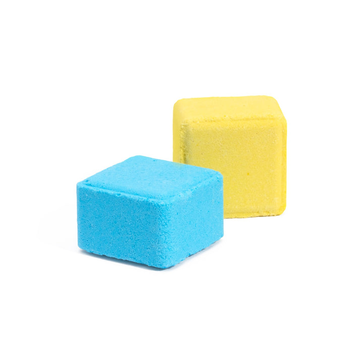 Close-up of 2 shower steamer tablets - 1 is yellow and is lemon sugar scented, infused with lemon essential oil for happiness. The other cube is blue, infused with royal jelly extract for confidence-boosting aromatherapy benefits