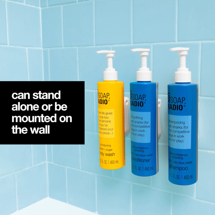 A blue tile shower as the background with a black box on the left hand side of the image containing white text stating "can stand alone or be mounted on the wall". To the right side of the text box one yellow and two blue Not Soap Radio bottles with a white pump cap and adhesive white wall mount are mounted on to the blue tile shower.