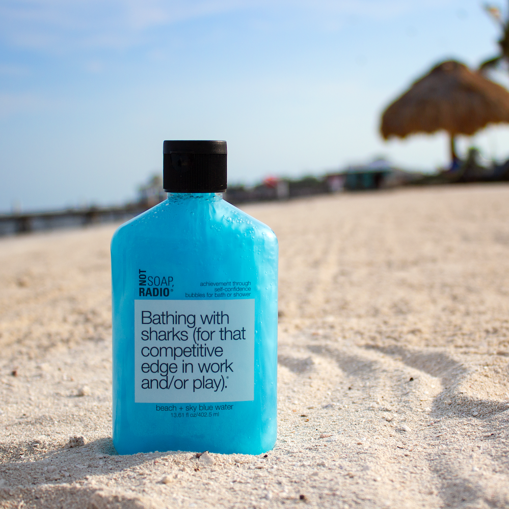 A blue colored bath and shower gel sitting in sand on a beach in Belize. 