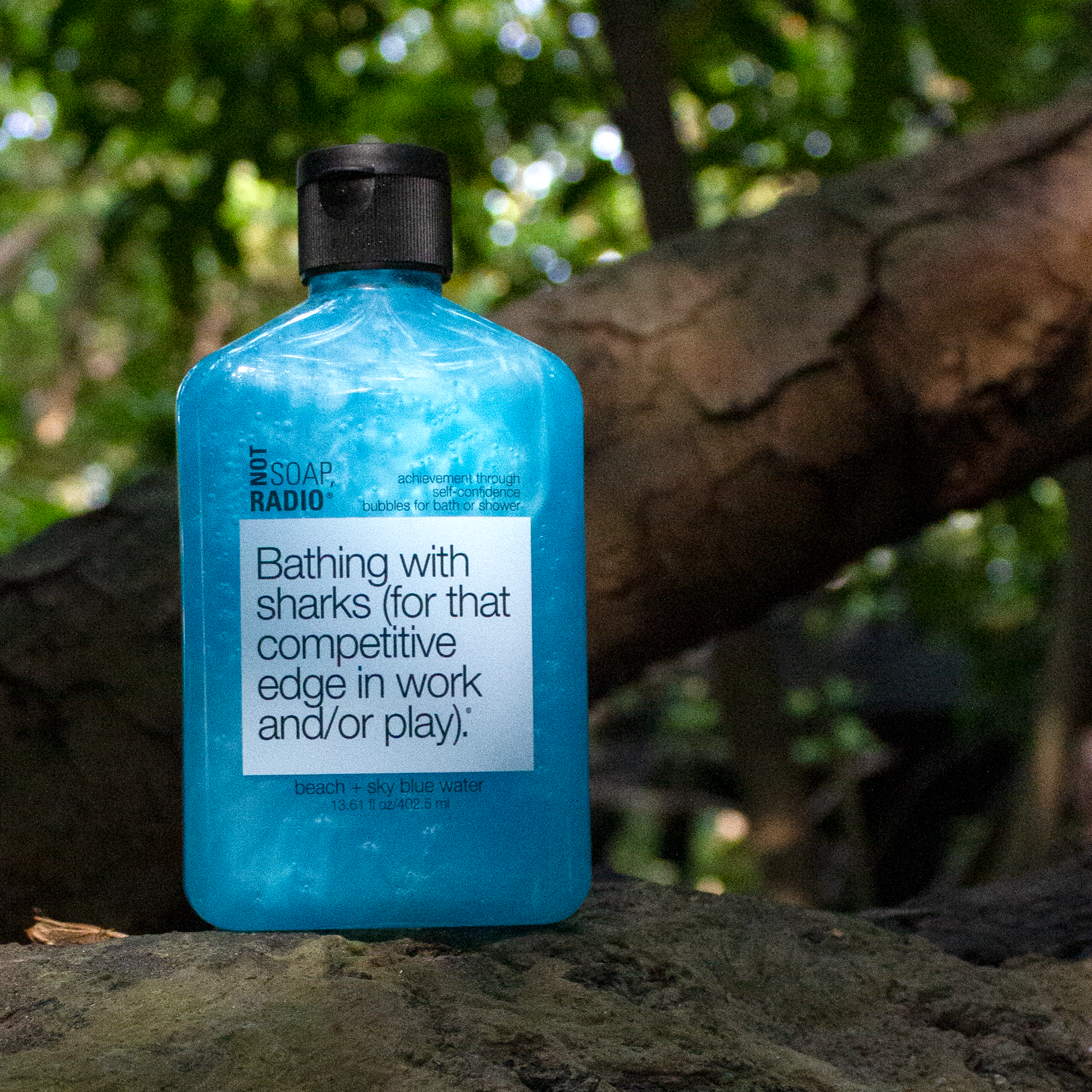 A light blue shower gel standing on top of a rock with a large tree branch in the background.