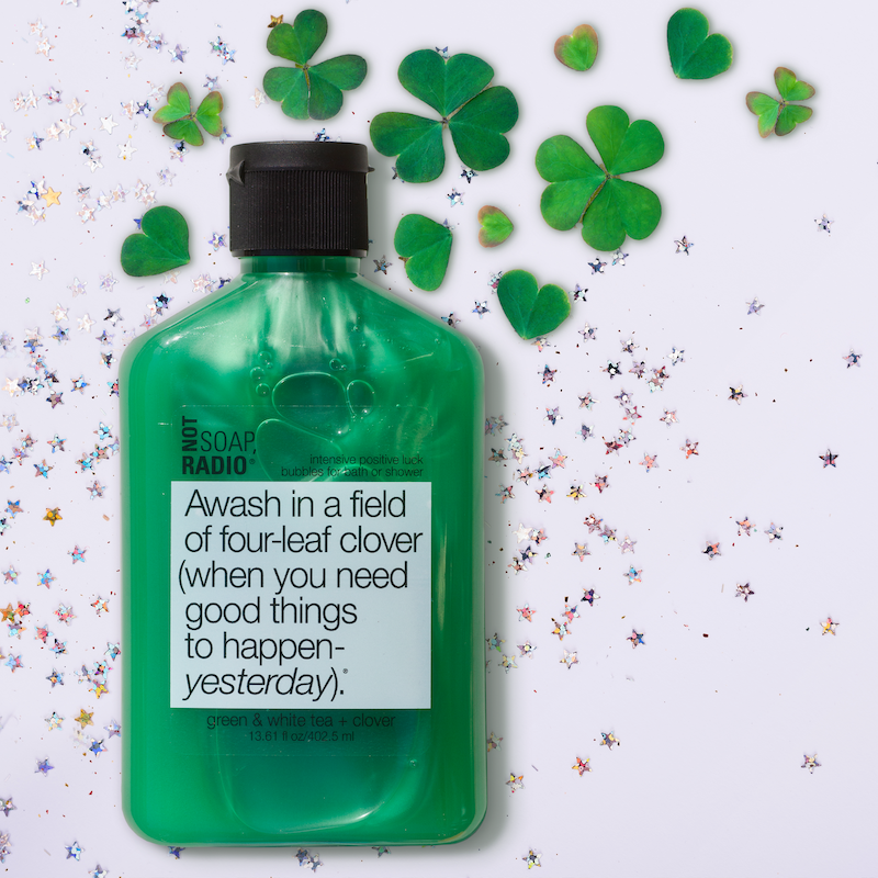 A green bubble bath shower gel flat lay on top on fluorescent stars and four leaf clovers.