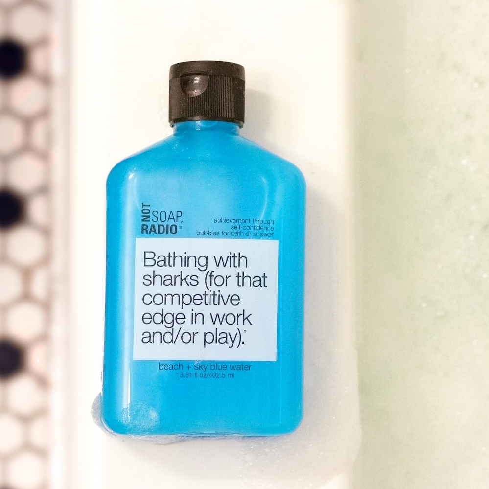 The Not Soap Radio "Bathing with sharks" shower gel laying on the side of a bathtub.