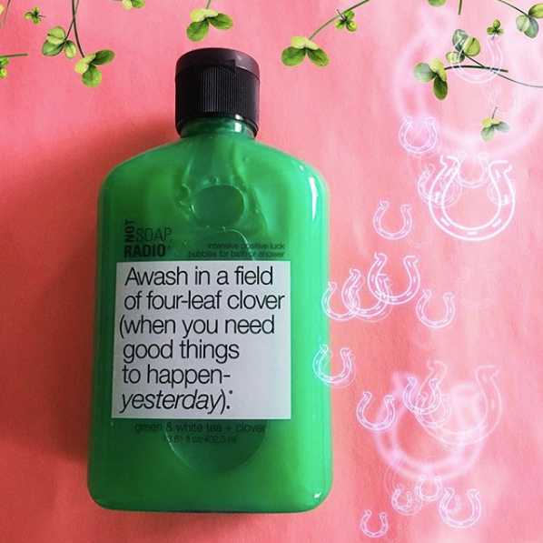 A good luck themed bath and body wash on a pink background with horseshoes and four leaf clovers surrounding the bottle.