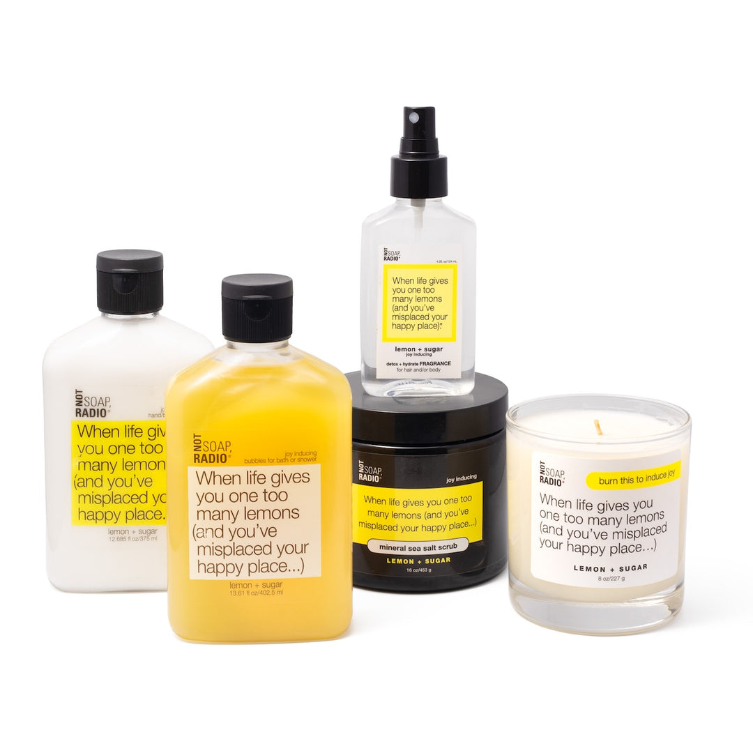 Lemon scented lotion, candle, shower gel, body mist, and sea salt scrub on a white background.