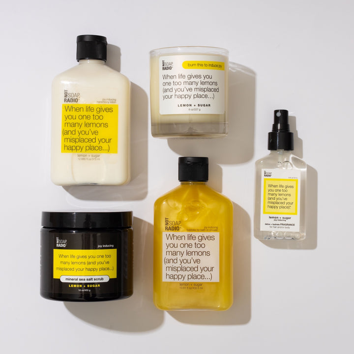 A flatlay of lemon sugar scented body lotion, mineral sea salt scrub, candle, bath/shower gel and fragrance spray.