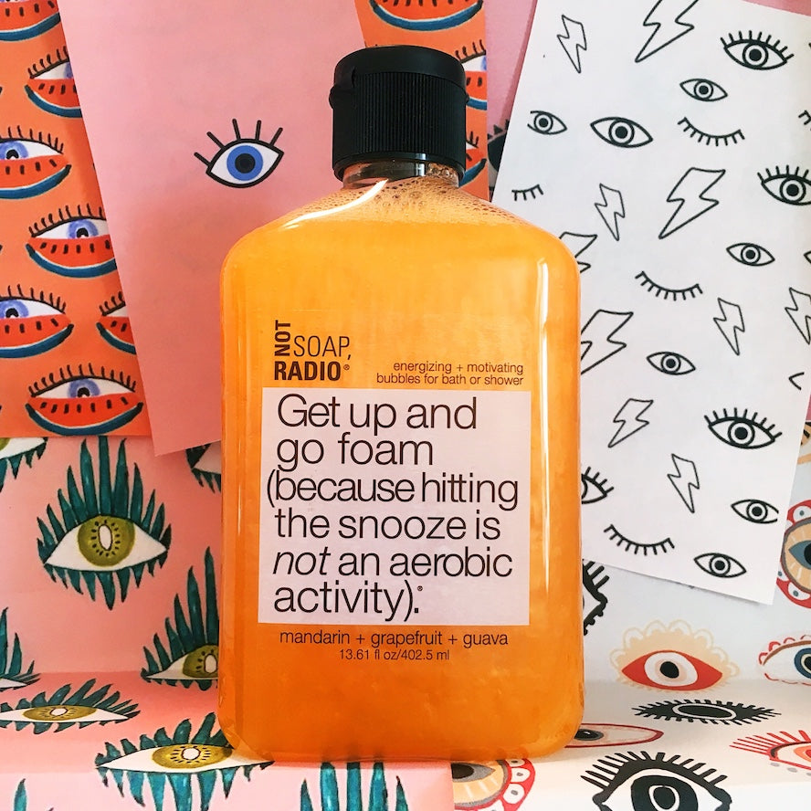 An orange colored bath and shower gel on top of collage cutouts of eyes.