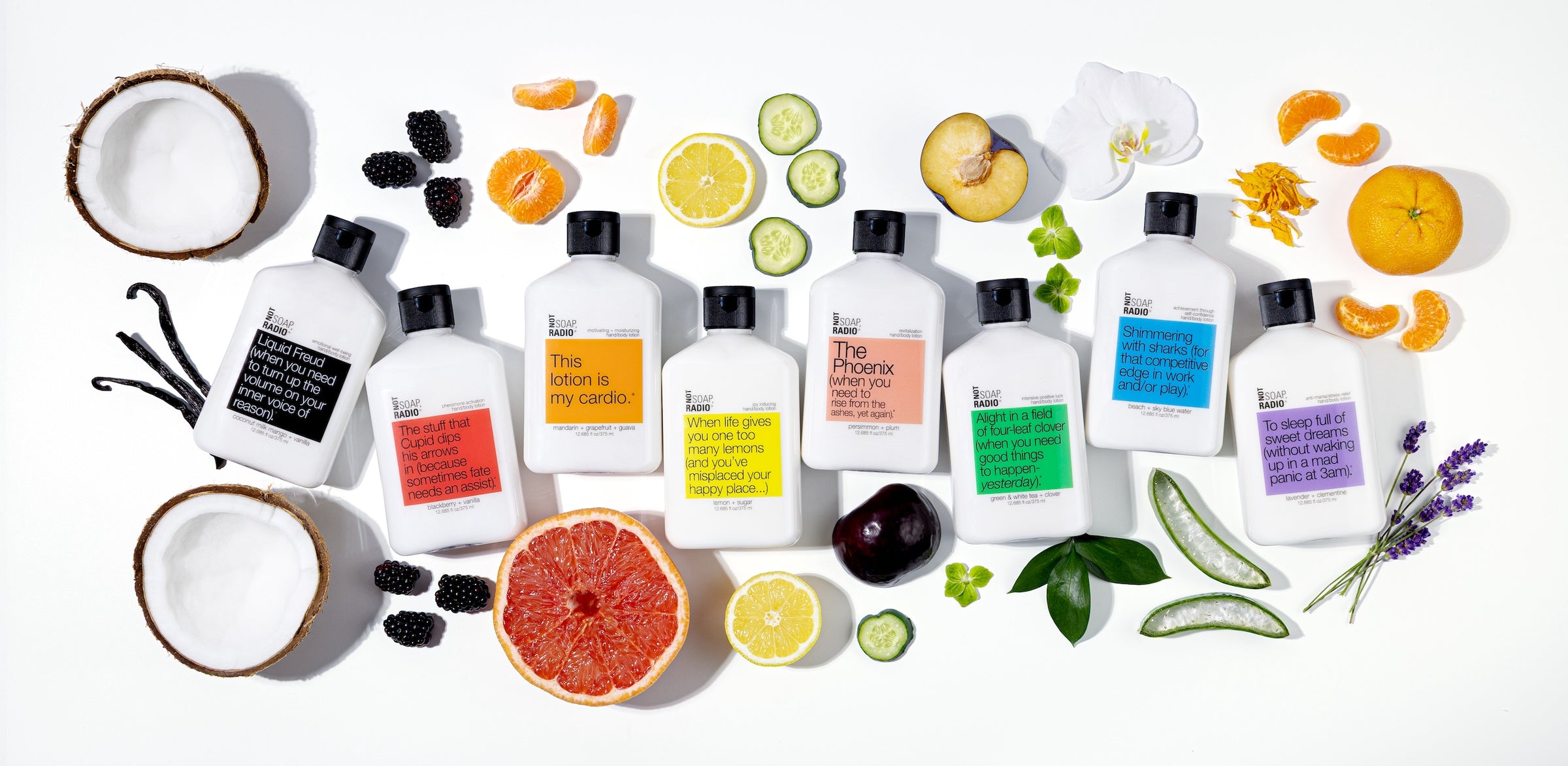 An array of 8 Not Soap Radio lotions laid out in a rainbow, surrounded with fresh fruits and botanical ingredients