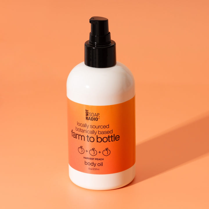 Harvest peach scented body oil by Not Soap Radio — locally sourced, botanically based formula in pink orange packaging, photographed on a bright peach background.