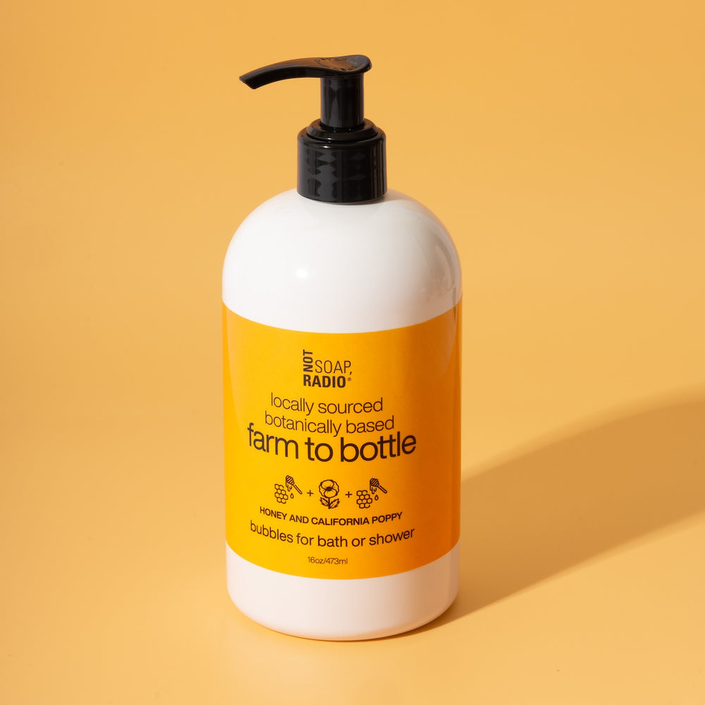 Not Soap Radio Farm to Bottle Honey and California Poppy bubbles for bath or shower — locally sourced, botanically based formula in amber-toned packaging, photographed on a warm yellow background.
