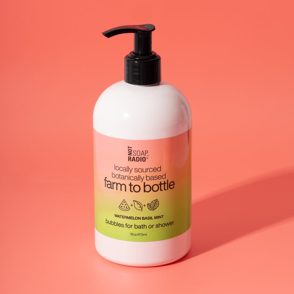 Not Soap Radio Farm to Bottle watermelon basil mint bubbles for bath or shower — locally sourced, botanically based formula in pink and green packaging, photographed on a bright pink background.