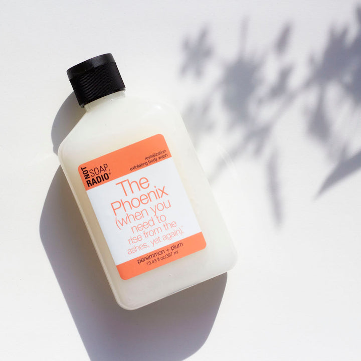 Not soap radio's persimmon and plum scented body scrub, flat laid on a white floral background