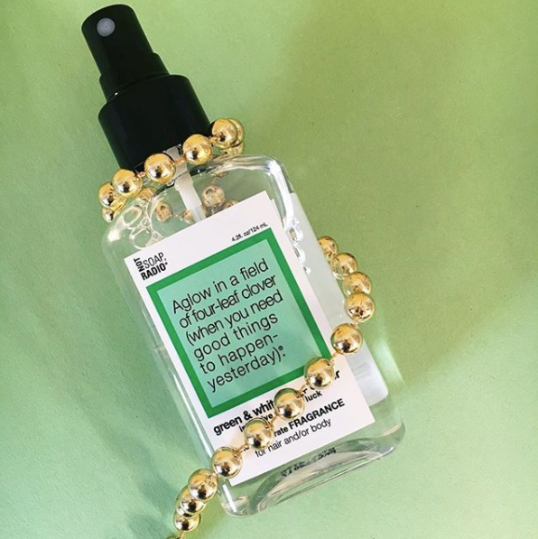 A green and white tea clover scented body mist with gold beads wrapped around it on a green background.