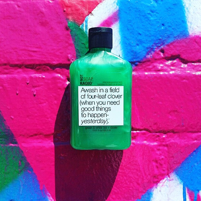 A green positivity shower gel laying on top of blue and pink painted bricks.
