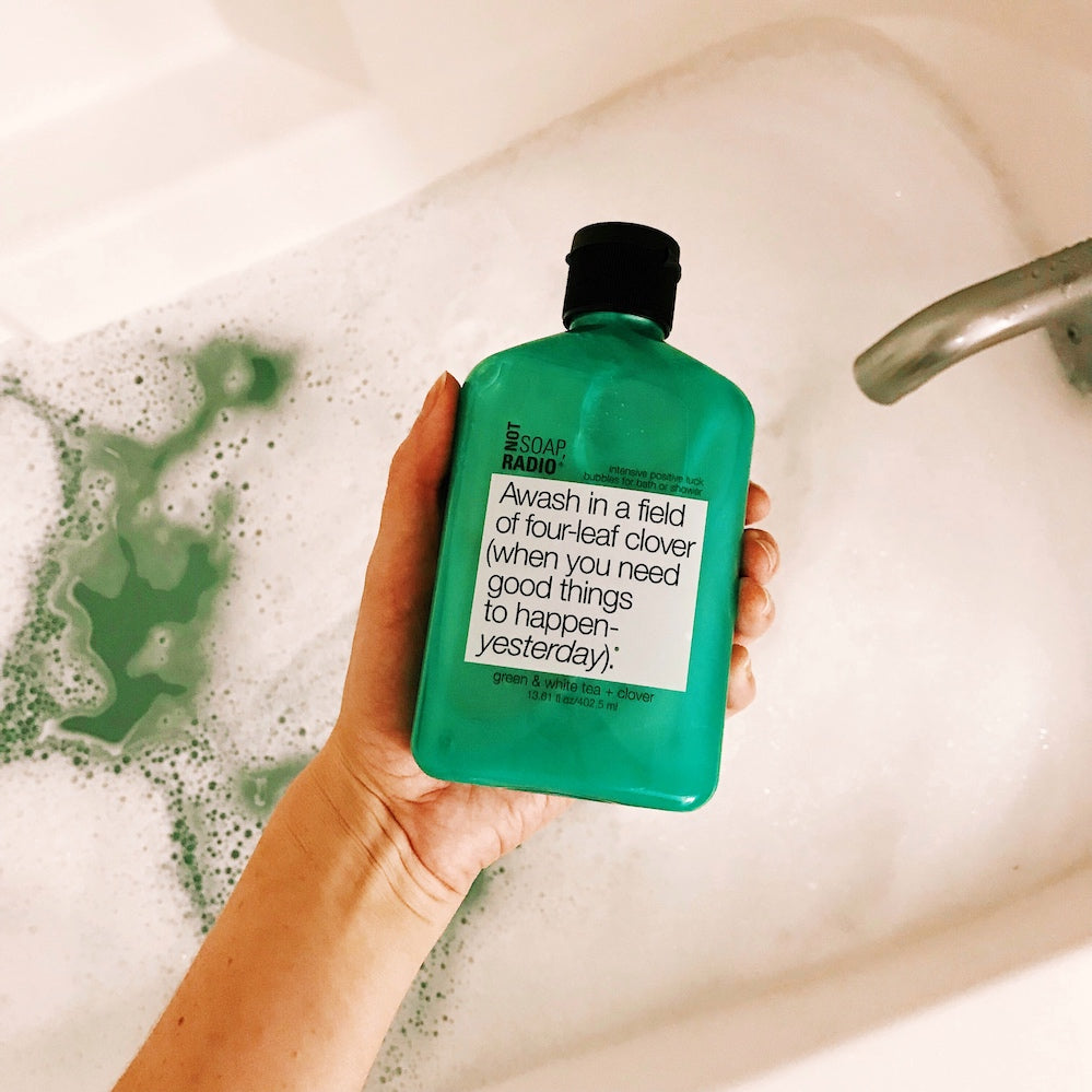 A green bubble bath gel being held over a bath filled with green bubbles.