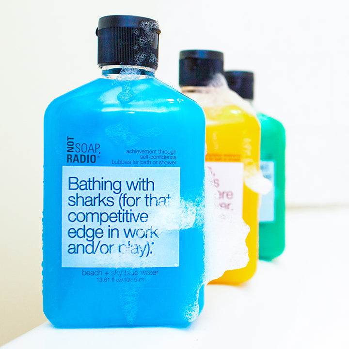 A bright blue bubble bath gel standing on the side of a bathtub with orange and green colored gels behind it.