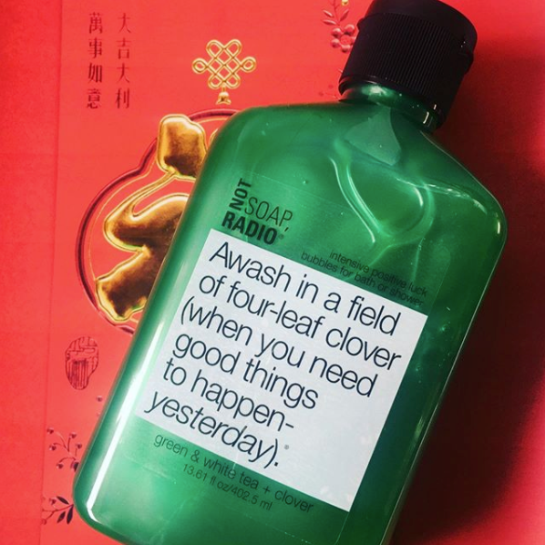 A green and white tea scented clover shower gel laying on top of a red Asian card about good luck.