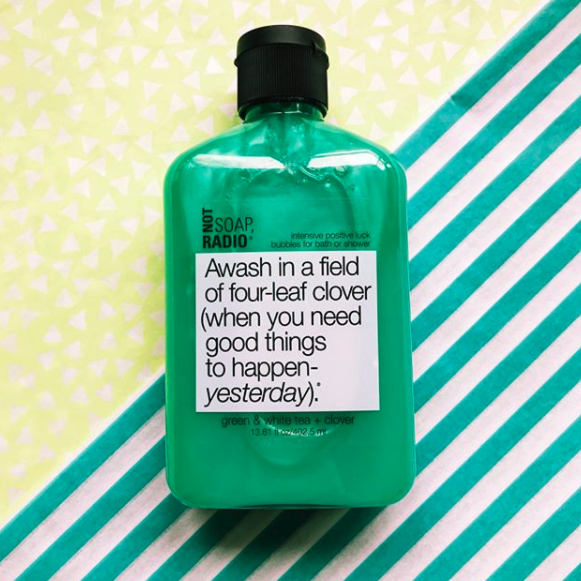 A green body wash laying on top of a green striped background that has yellow stars next to it.