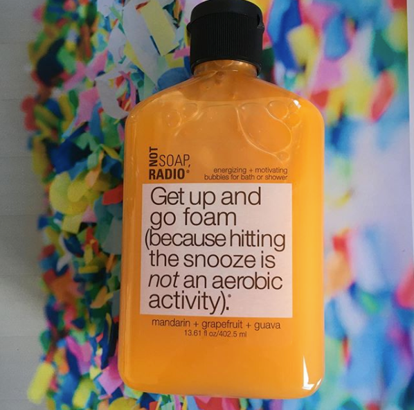 A mandarin orange colored bath and shower gel on top of colorful paper clippings.